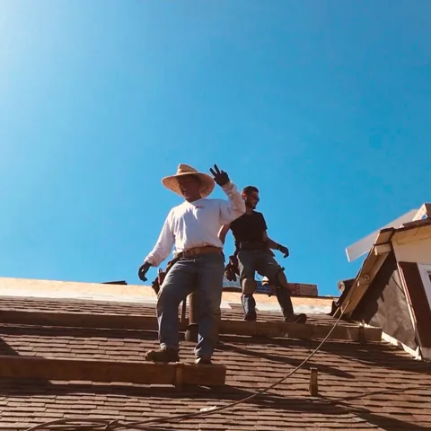 Two roofers standing on a wood shake roof, one waving