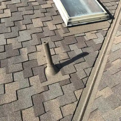 Stone coated pipe beside a skylight and valley on a brown shingle roof